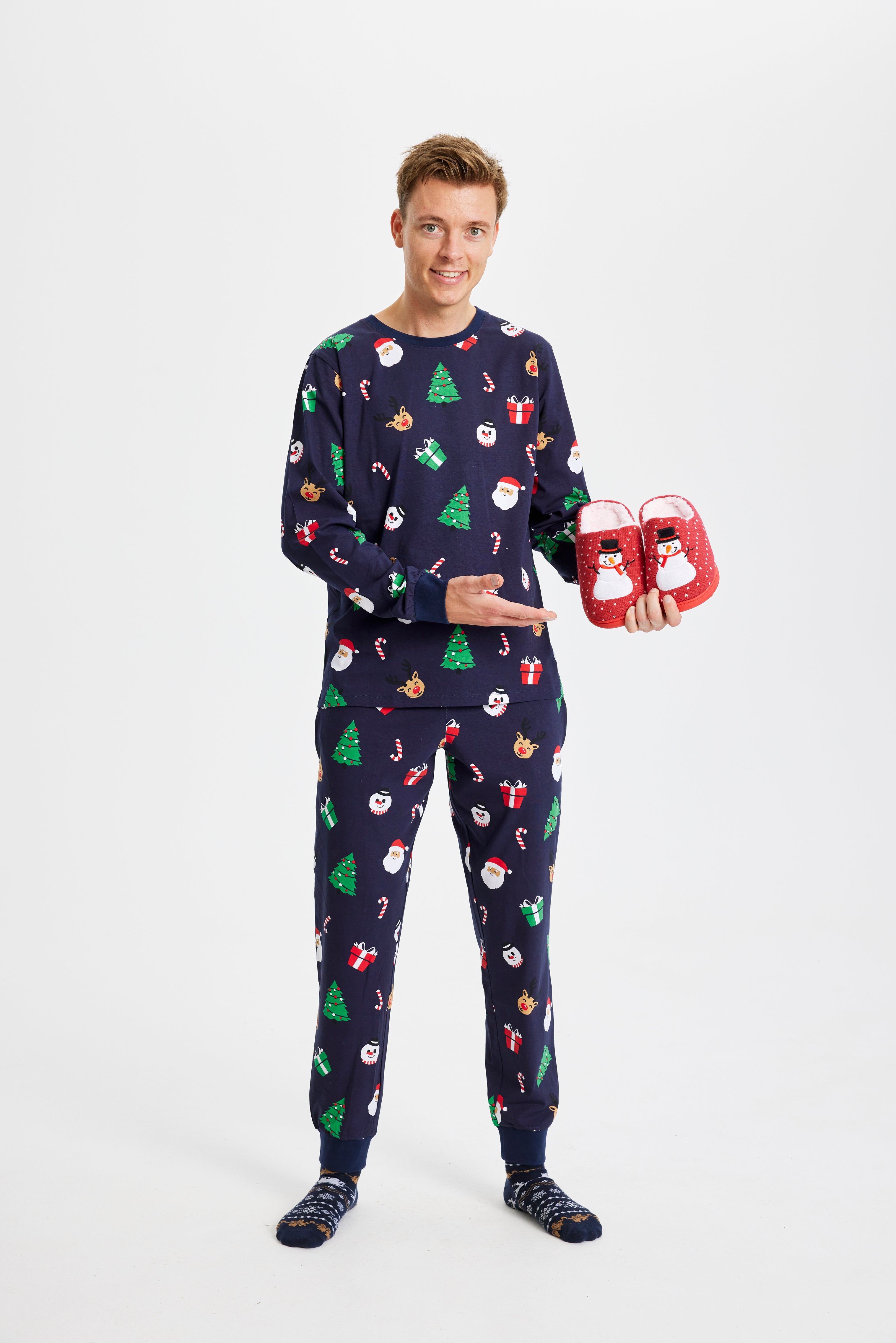 Eine überraschte Frau mit einem Geschenk in einem blauen Weihnachtspyjama mit Weihnachtsbäumen.